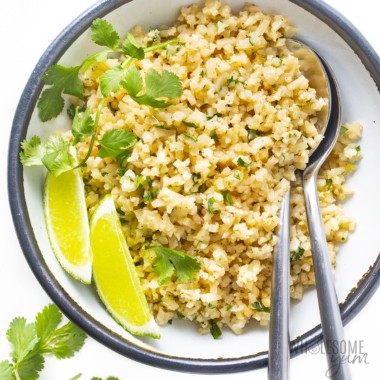 Cilantro lime cauliflower rice in a serving bowl with lime wedges
