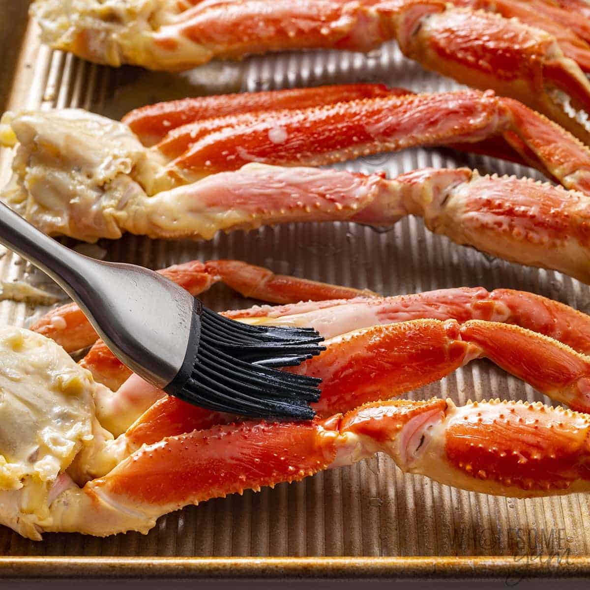 Broiled crab legs being brushed with butter