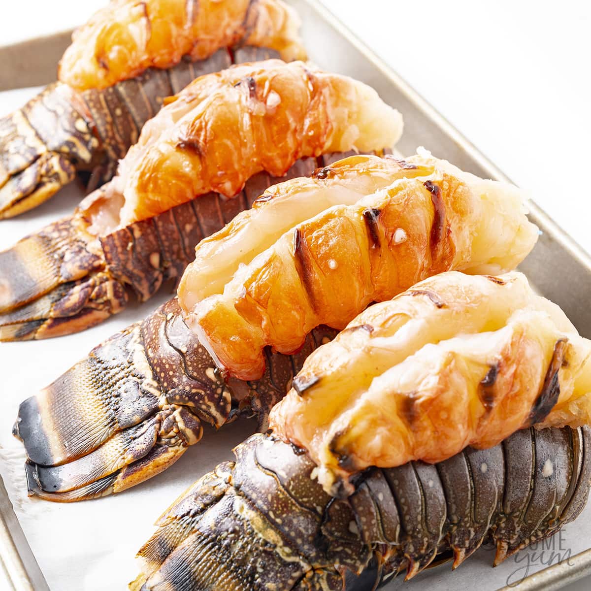 Butterflied lobster tails on a baking sheet.