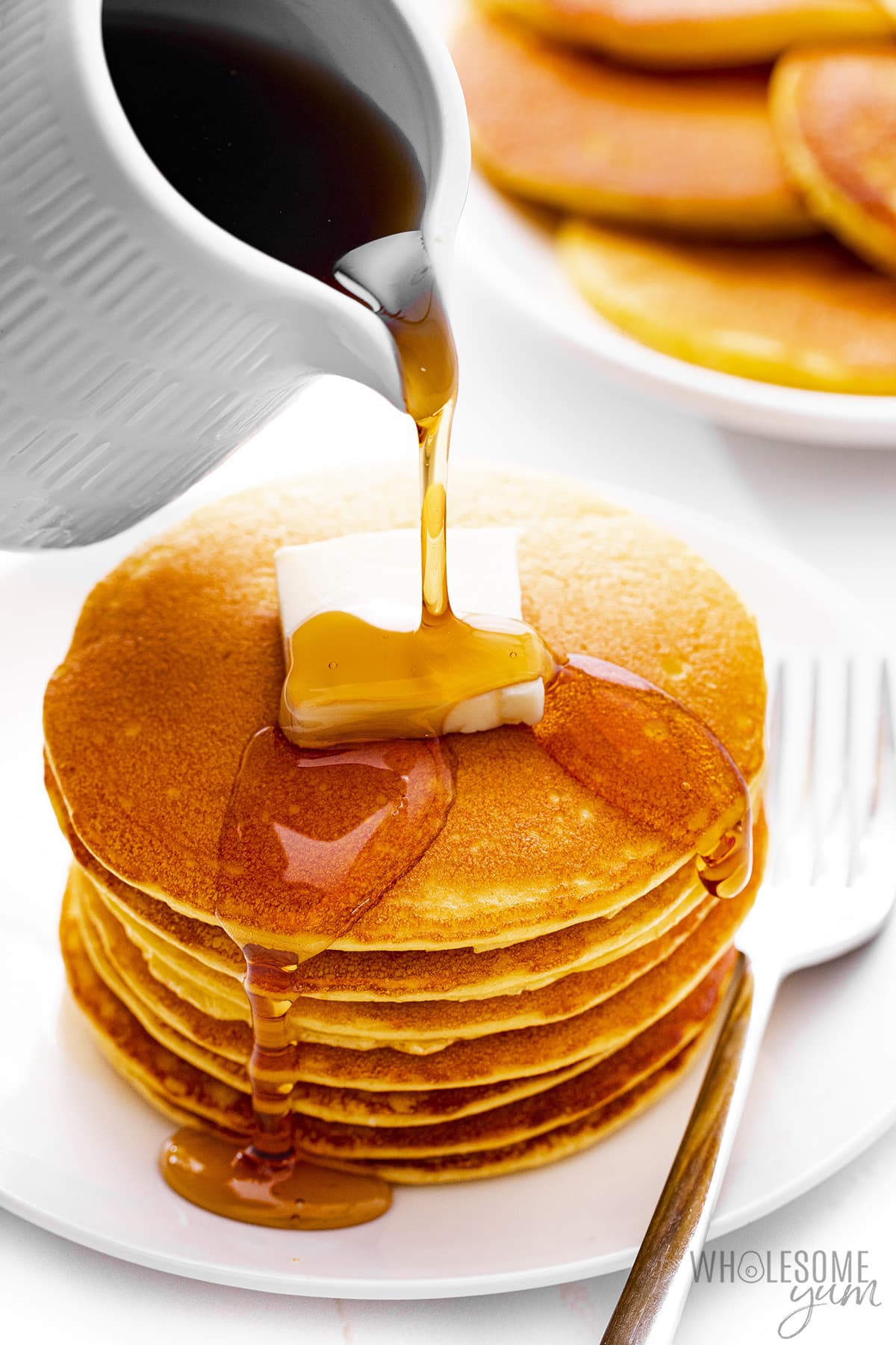 Pouring syrup over a stack of coconut flour pancakes.