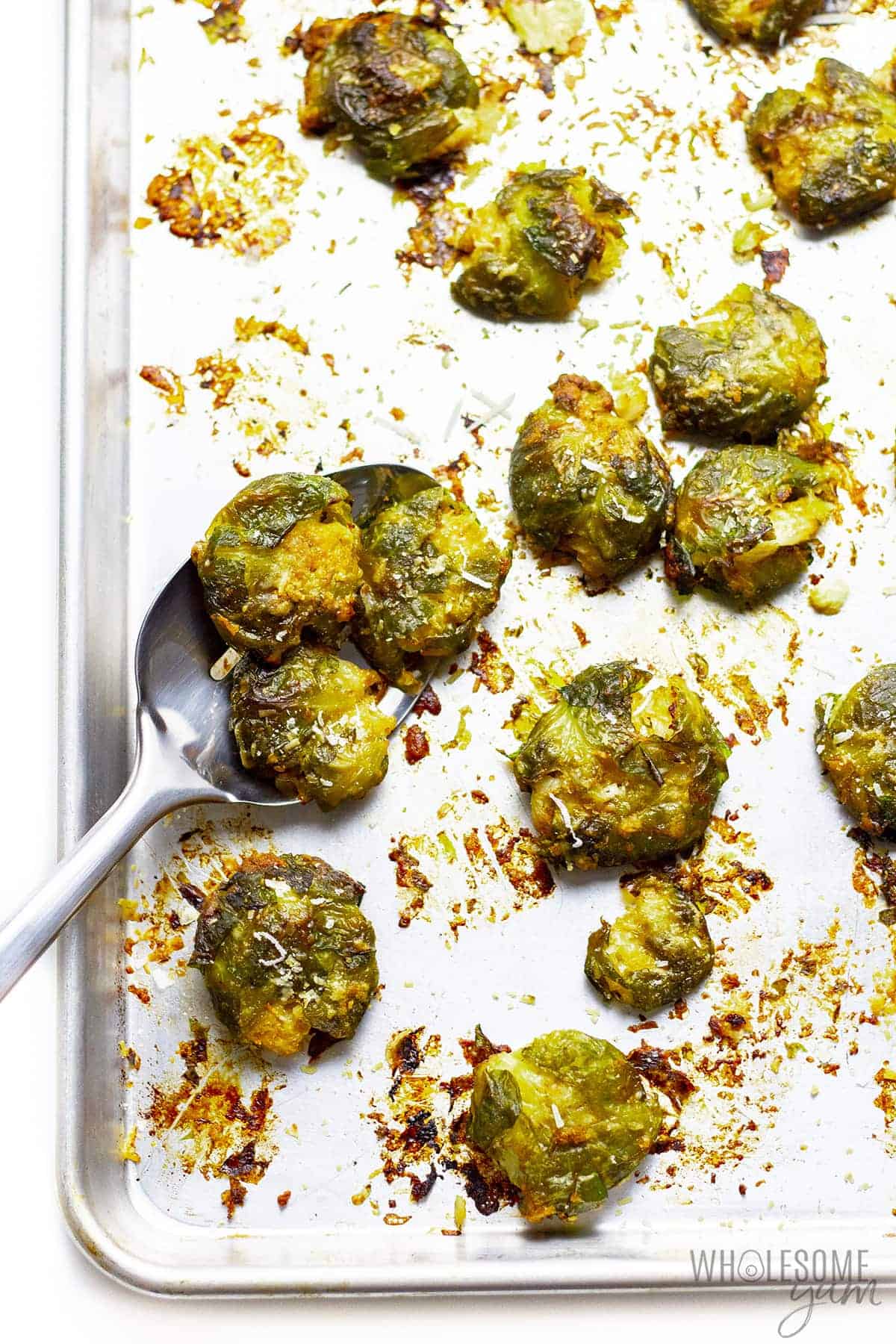Crispy smashed brussels sprouts on sheet pan with a serving spoon.