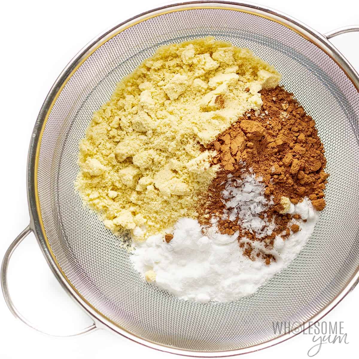Dry ingredients for keto macarons in a sifter over a mixing bowl