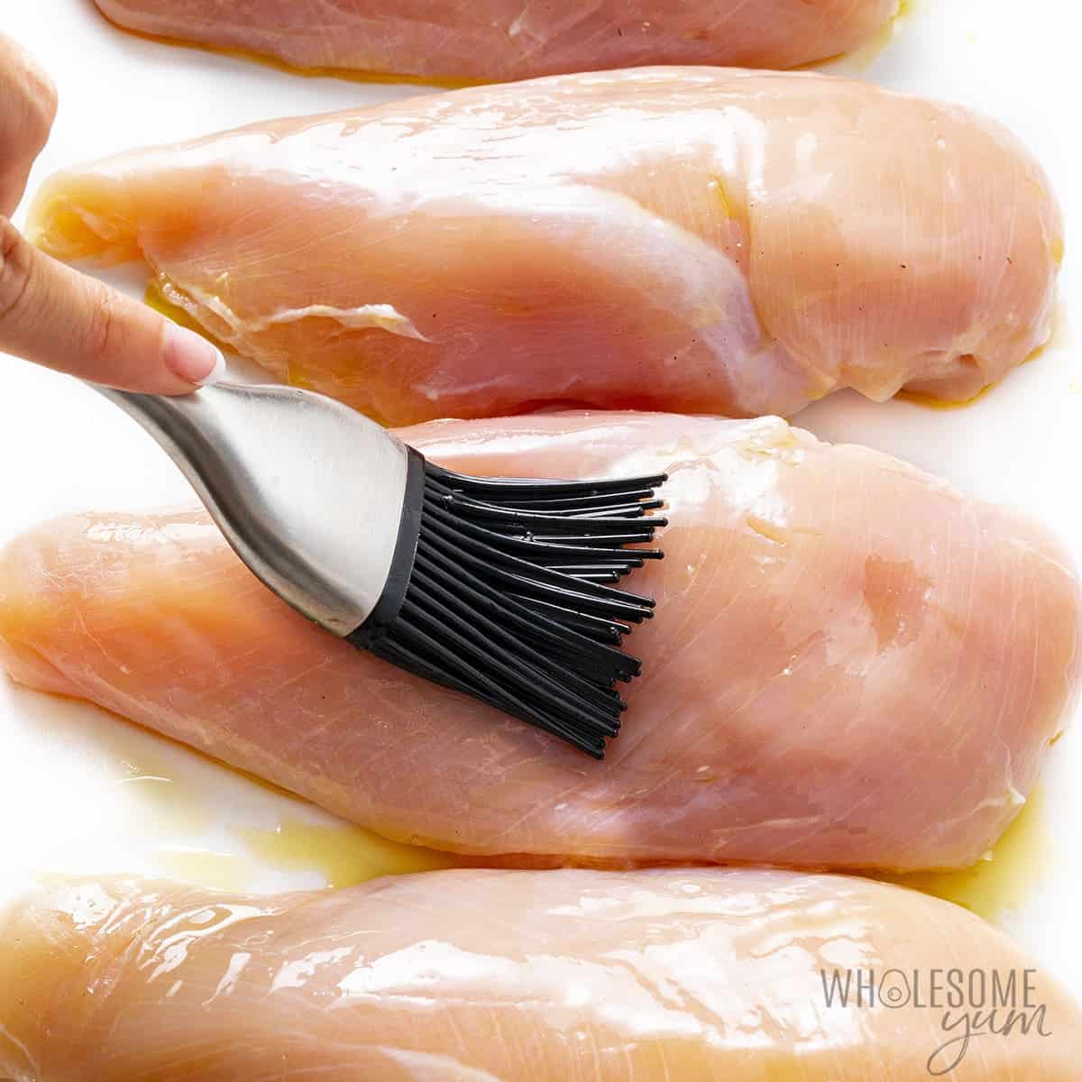 Brushing chicken breasts with olive oil