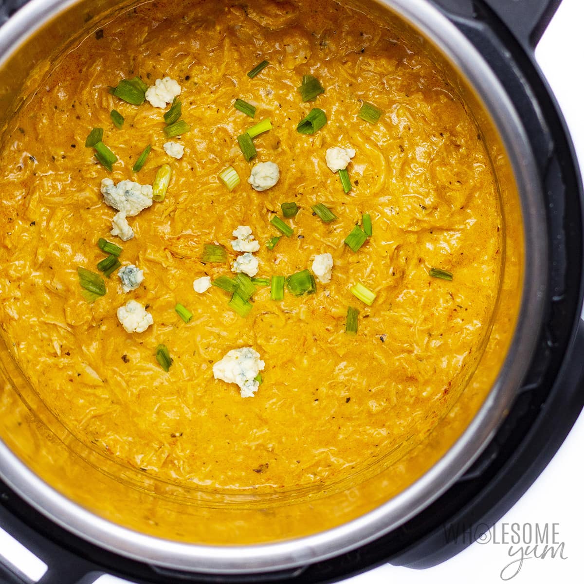 Buffalo chicken dip in the Instant Pot with garnishes on top.