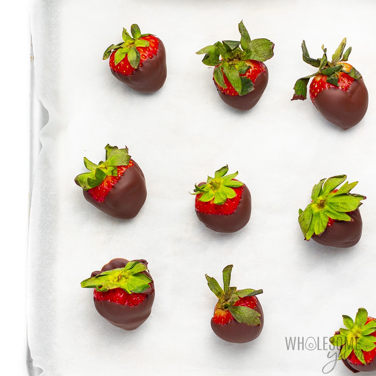 Sugar-free chocolate covered strawberries on a parchment lined baking sheet.