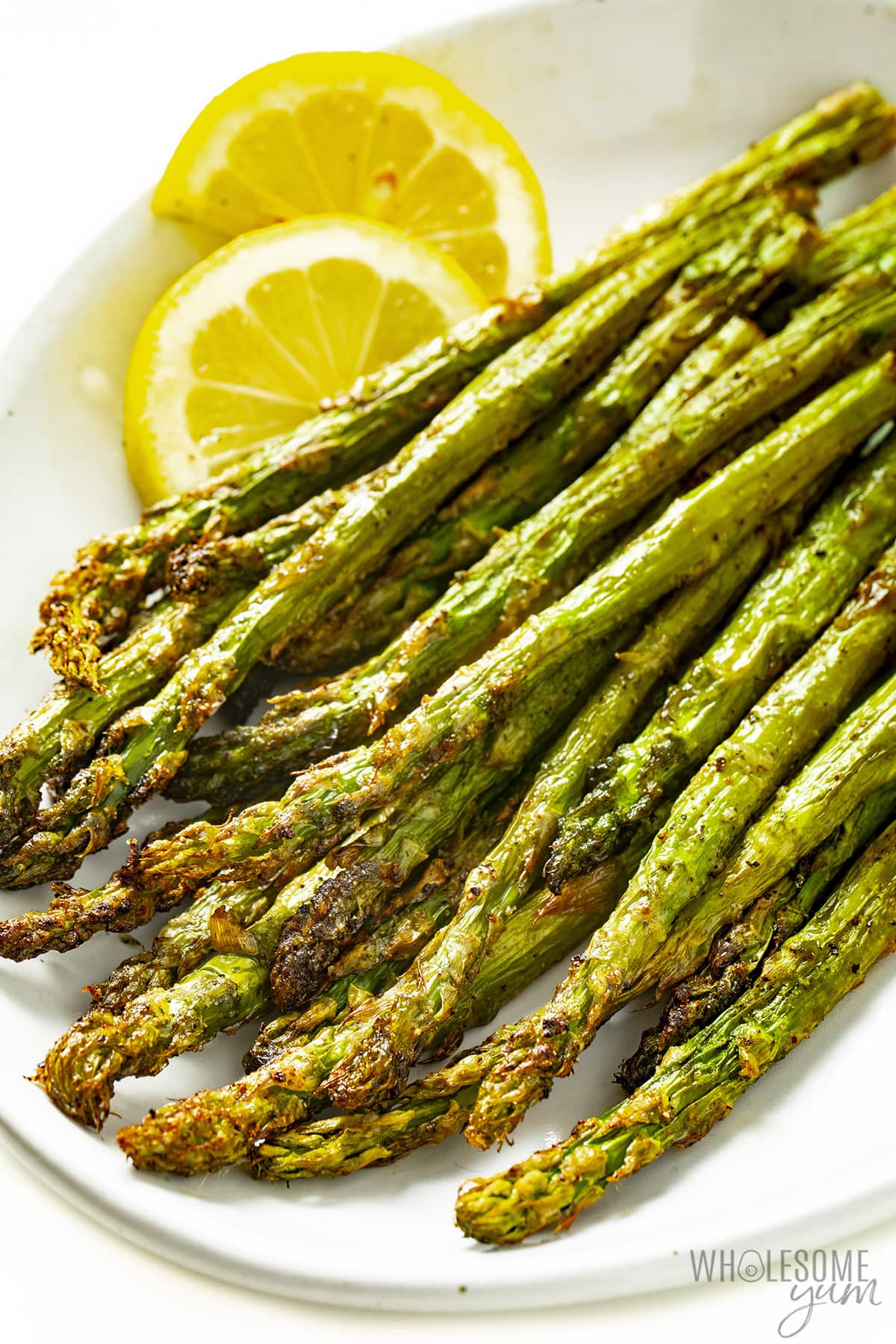 Plate of air fried asparagus with lemon wedges.