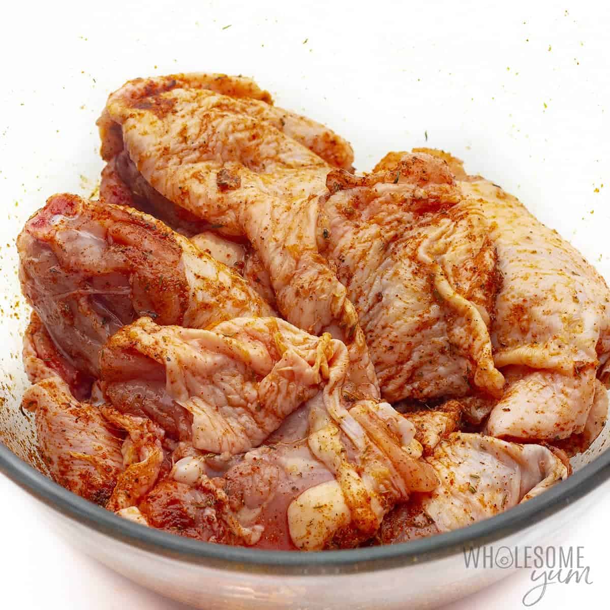 Chicken with seasonings coating the skin in a glass bowl.