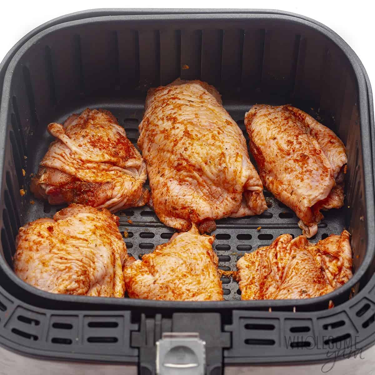 Raw chicken thighs in the air fryer basket.
