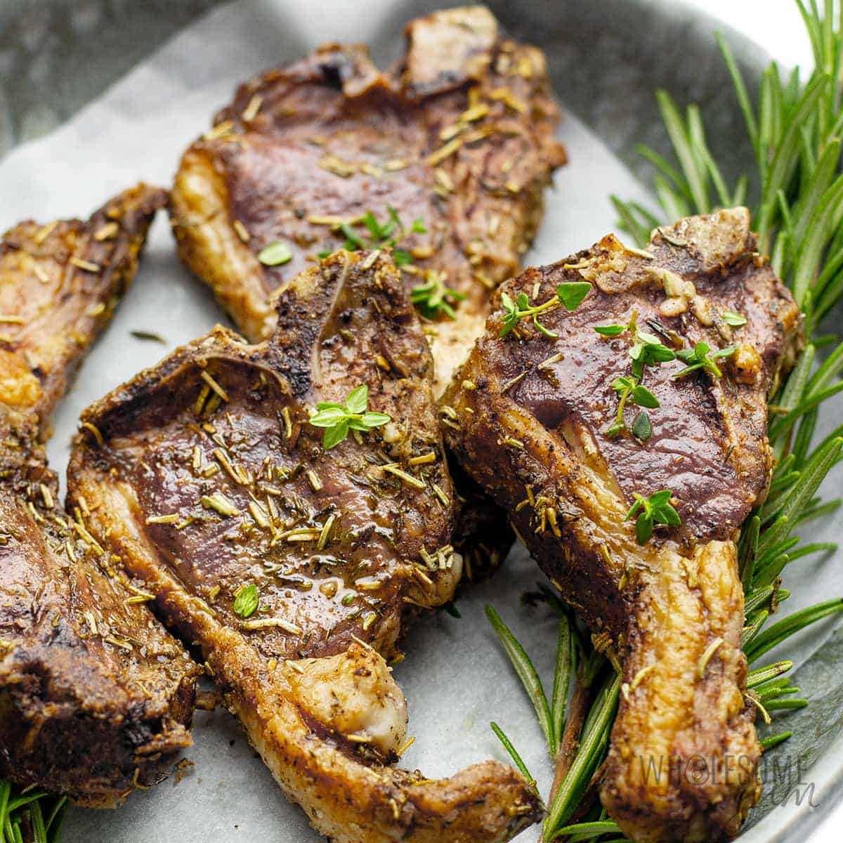Air fryer lamb chops on a plate with fresh rosemary.