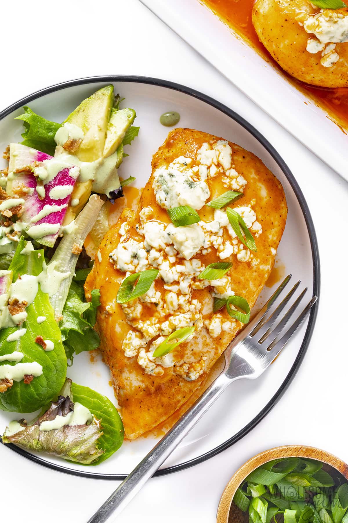 Baked buffalo chicken breast on a plate with green goddess salad.