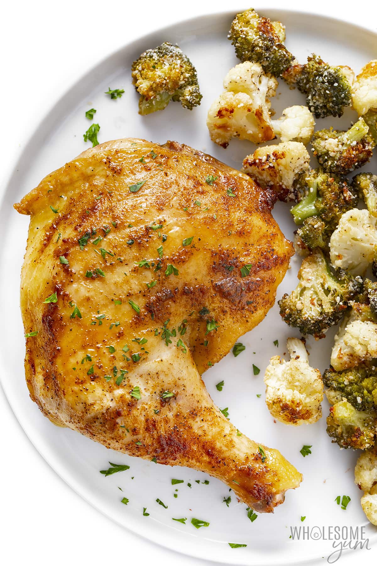 Oven baked chicken leg quarters plated with broccoli and cauliflower.