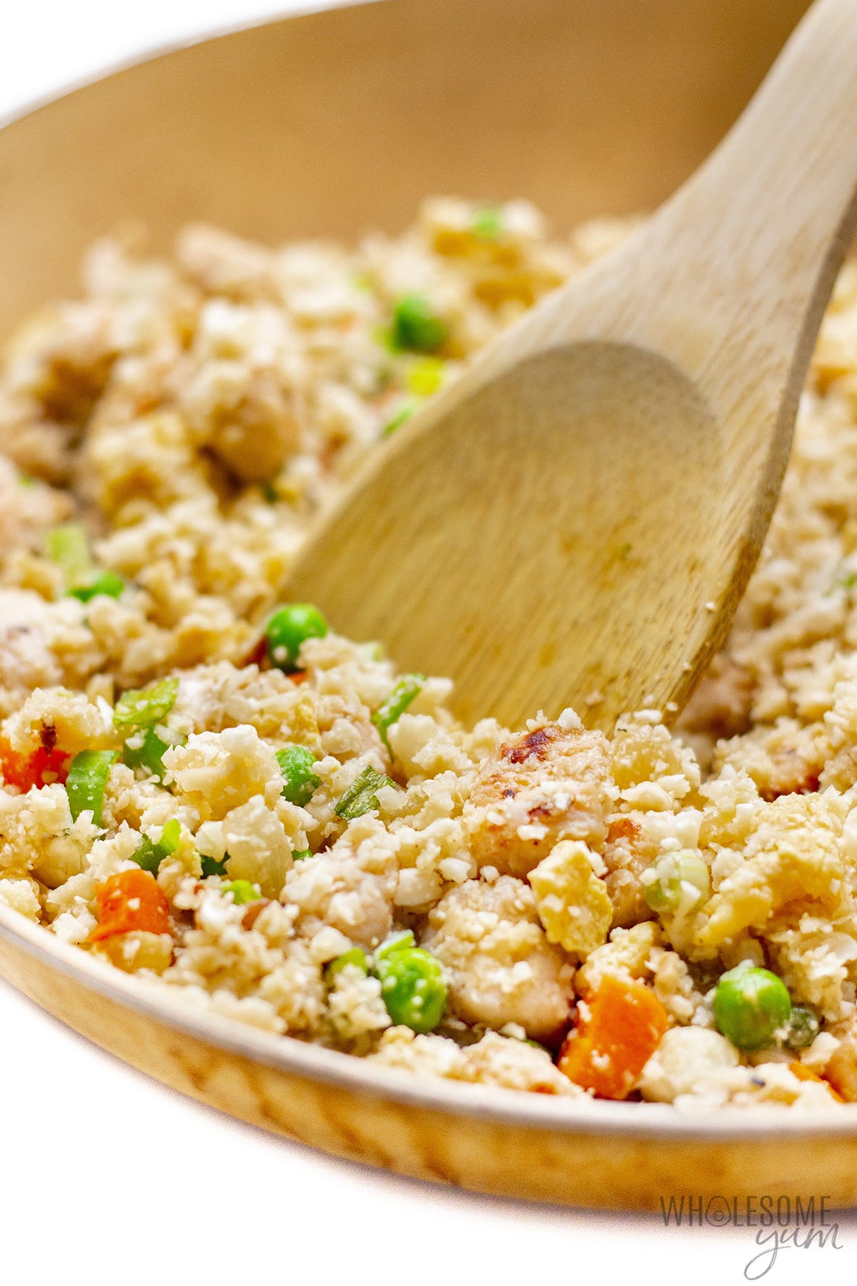 Closeup of cauliflower chicken fried rice with a wooden spoon.