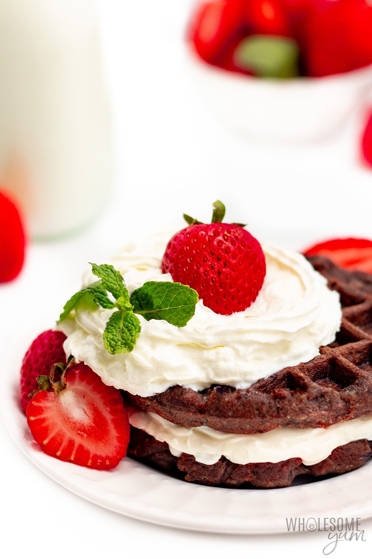 Side view of a chocolate cream cheese chaffle with strawberries and milk in background