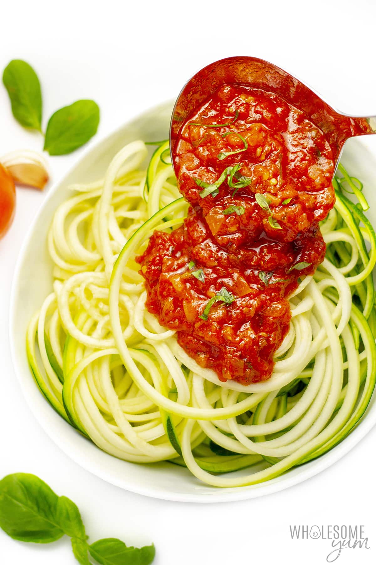 Spooning keto pasta sauce over zucchini noodles.