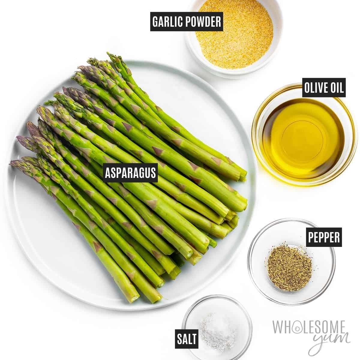 Bunch of asparagus on a plate with olive oil and seasonings next to it.