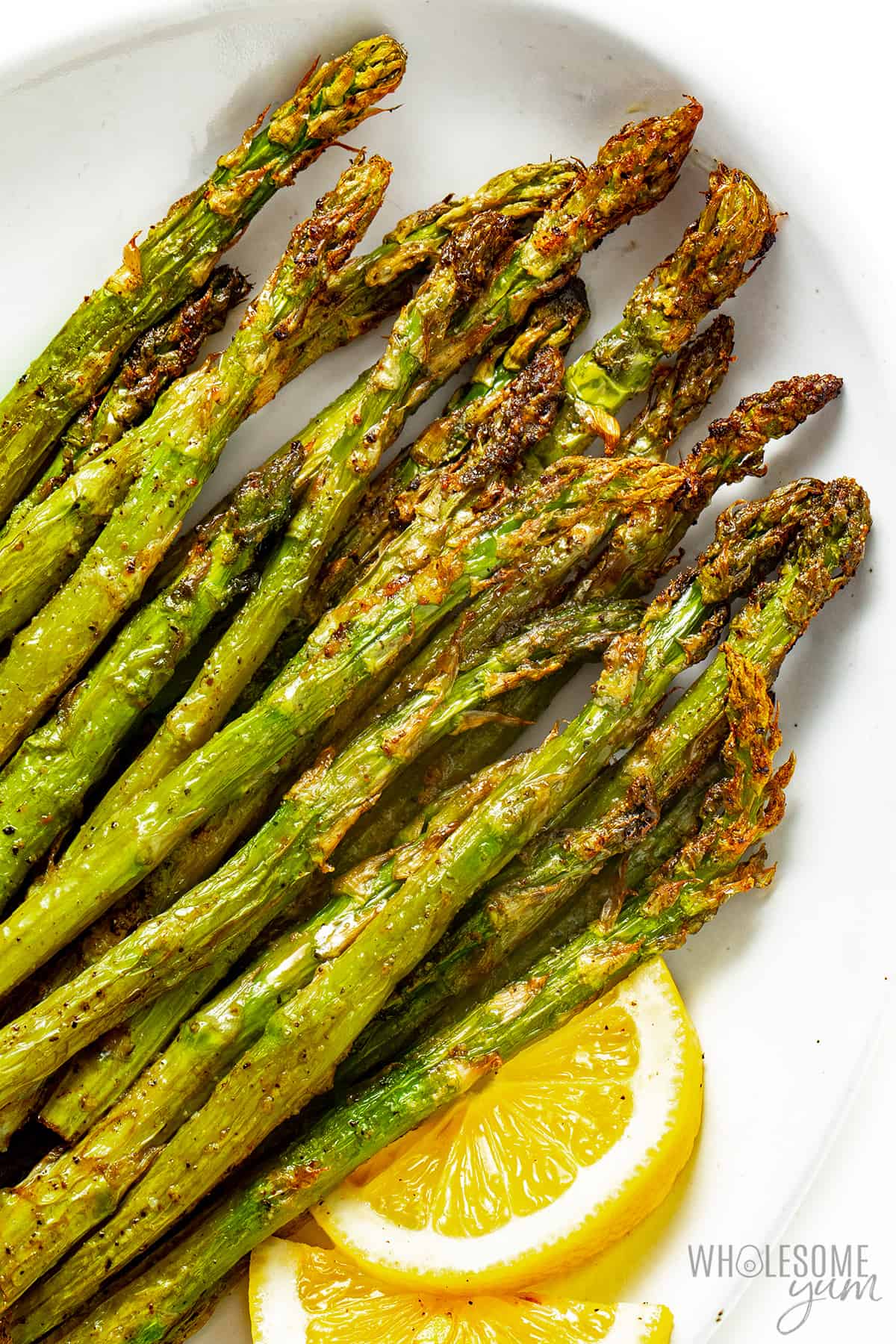 Plate of asparagus cooked in air fryer with lemon wedges.