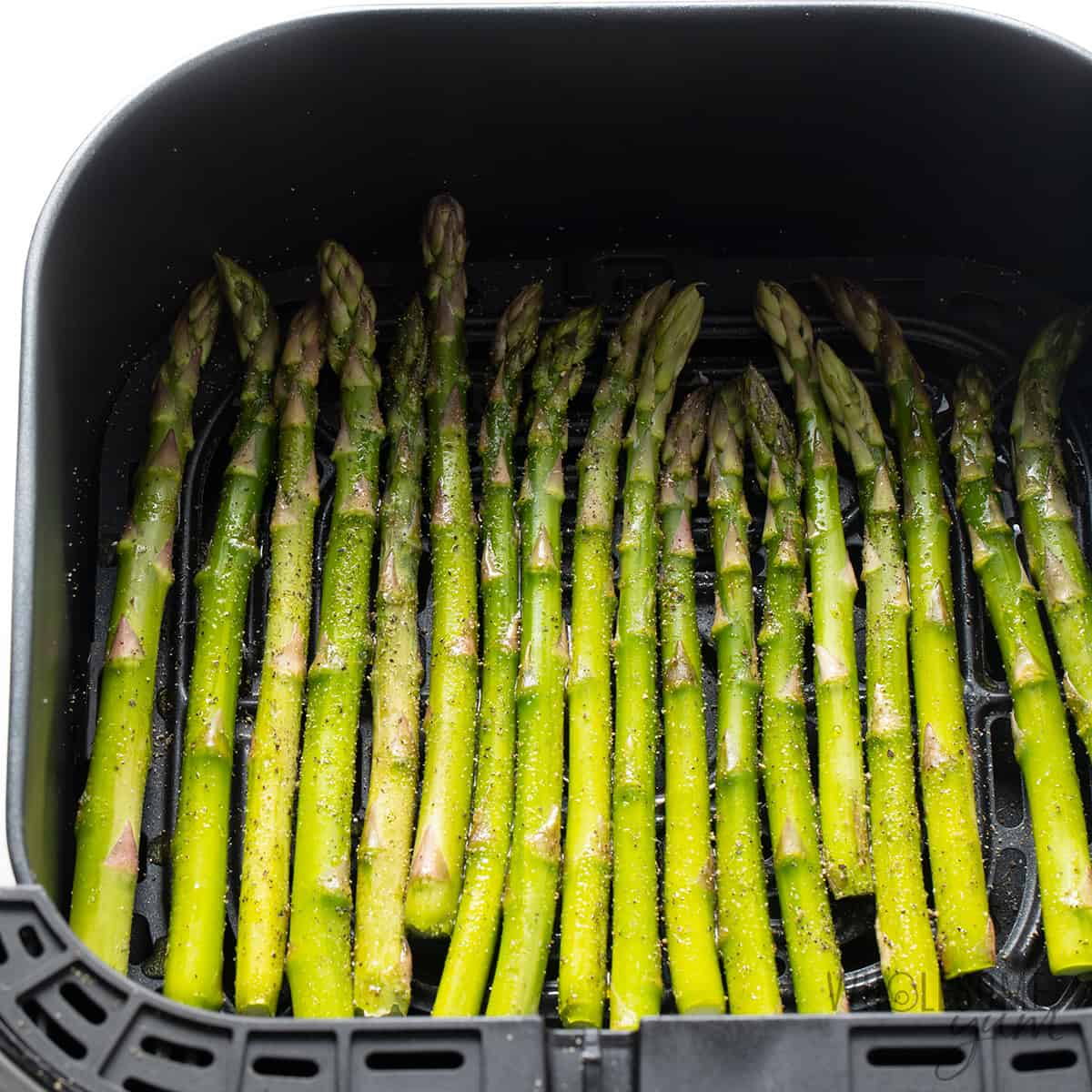 Seasoned asparagus in air fryer basket.