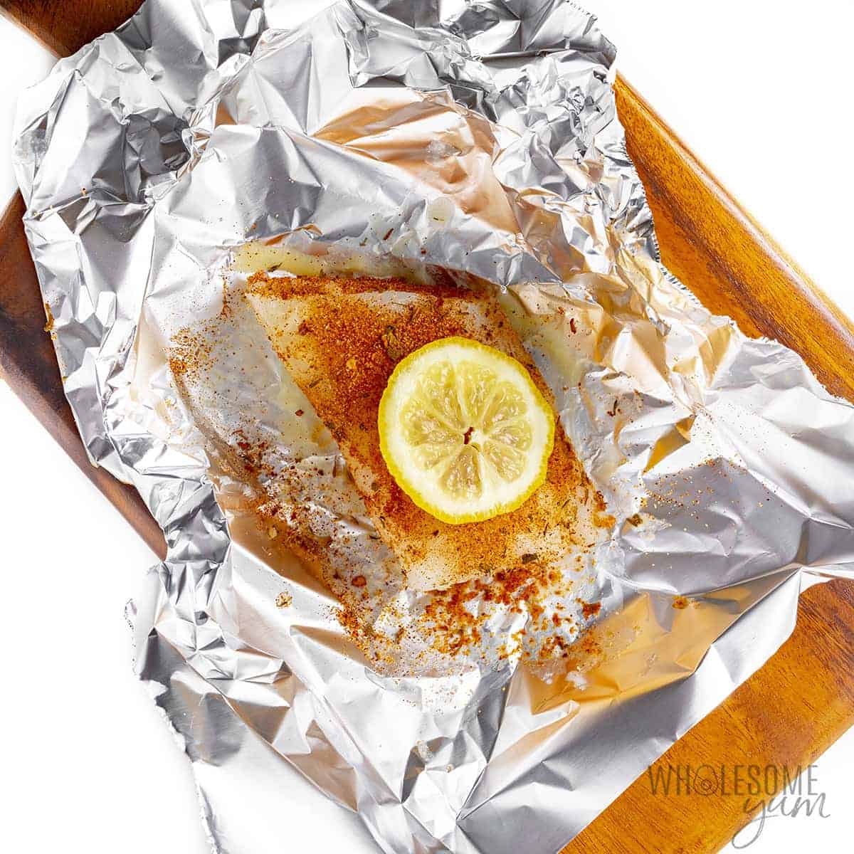 Seasoned raw cod fillet with lemon slice on top.