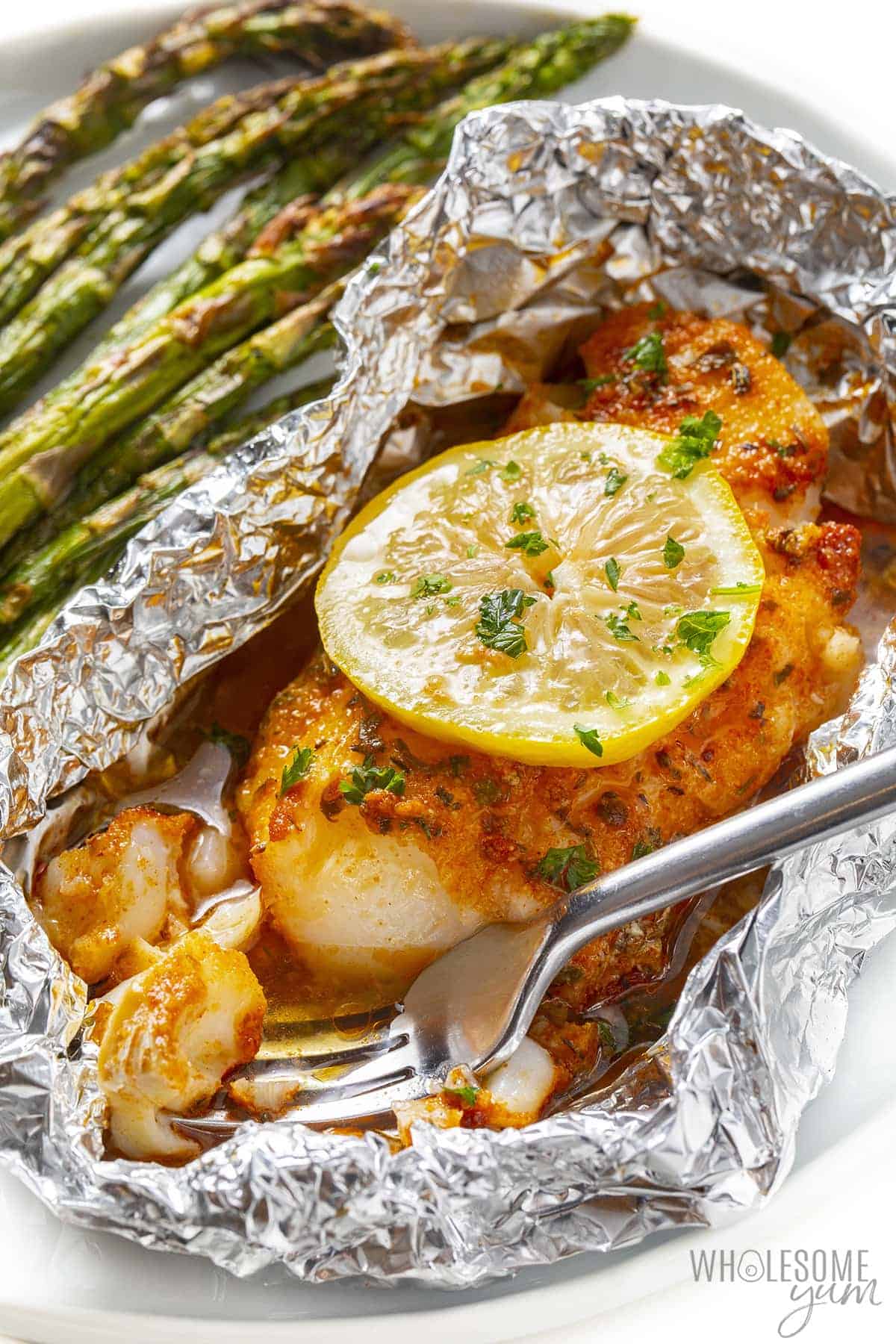 Grilled cod in foil on a plate with asparagus.