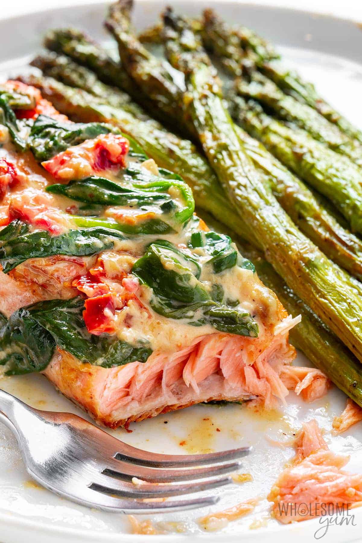 Garlic Tuscan salmon flaked with a fork and asparagus on the side.