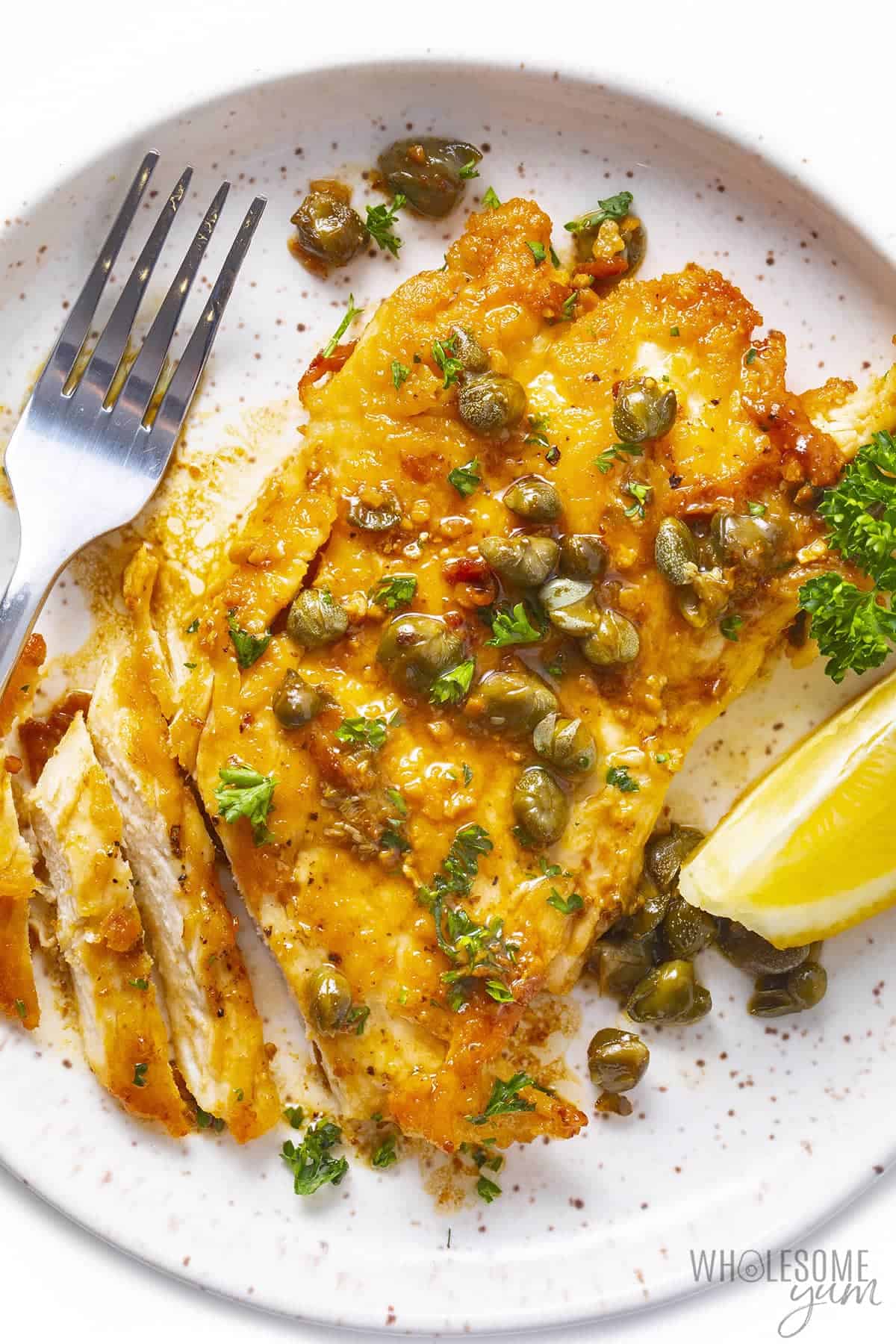 The lemon chicken piccata is plated and sliced ​​next to a fork.