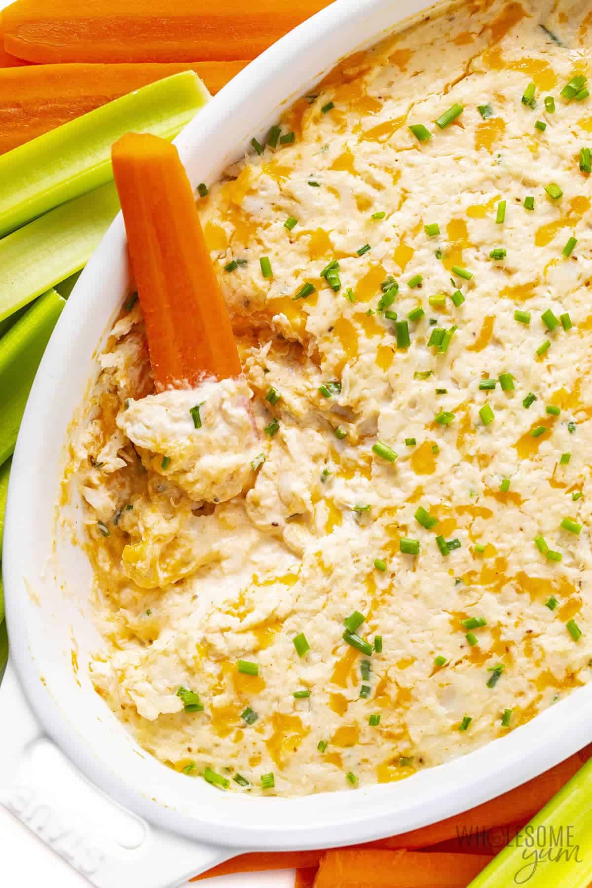 Baked hot crab dip on a platter with carrots and celery.