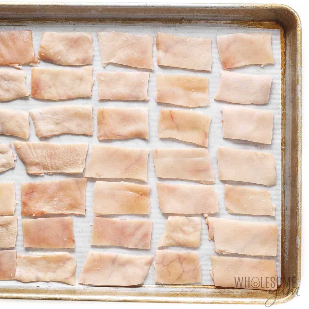 Unbaked pork rinds arranged on baking sheet.