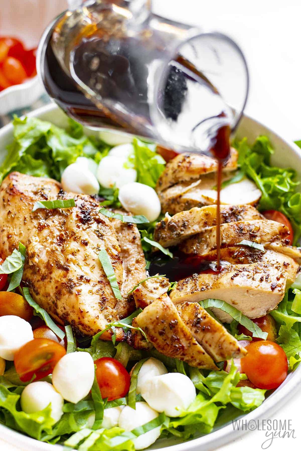 Balsamic glaze pouring over caprese salad with chicken.