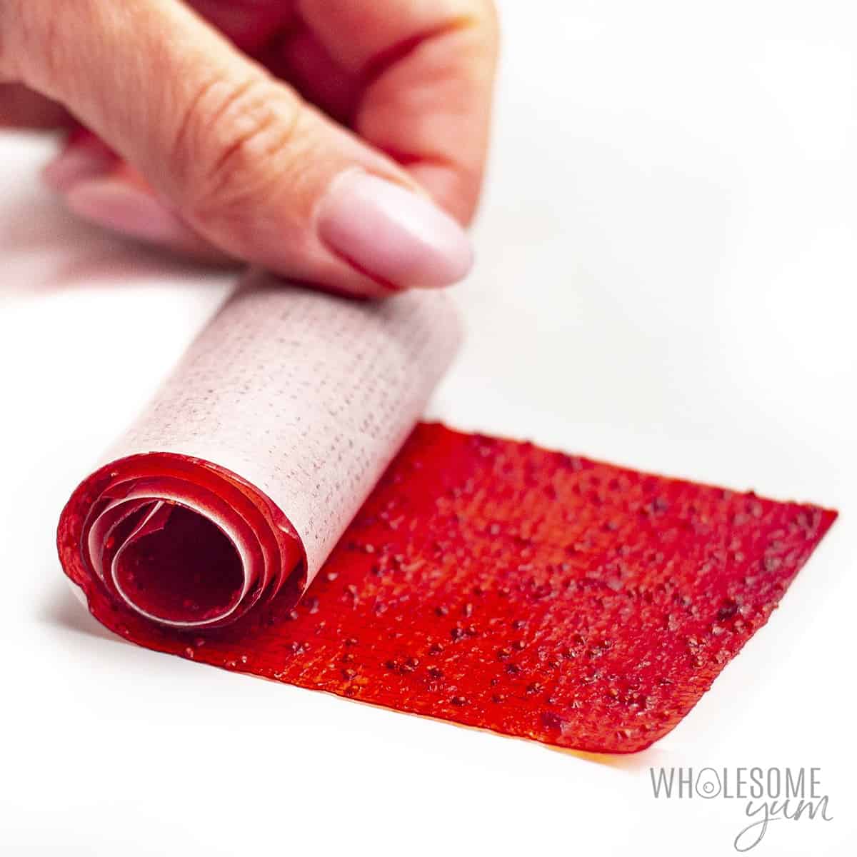 Hand rolling fruit leather into rolls with parchment facing out.