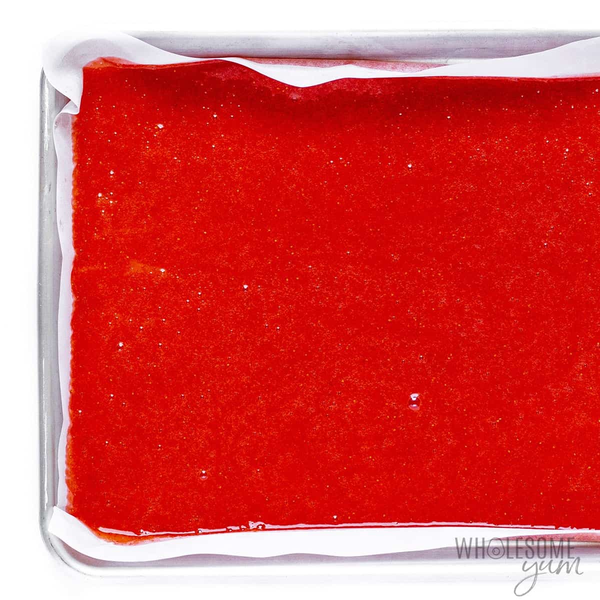 Fruit puree spread out on parchment lined pan.