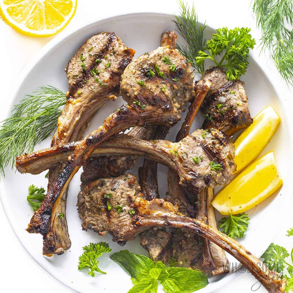 Grilled lamb chops with fresh herbs and lemon wedges on a platter.