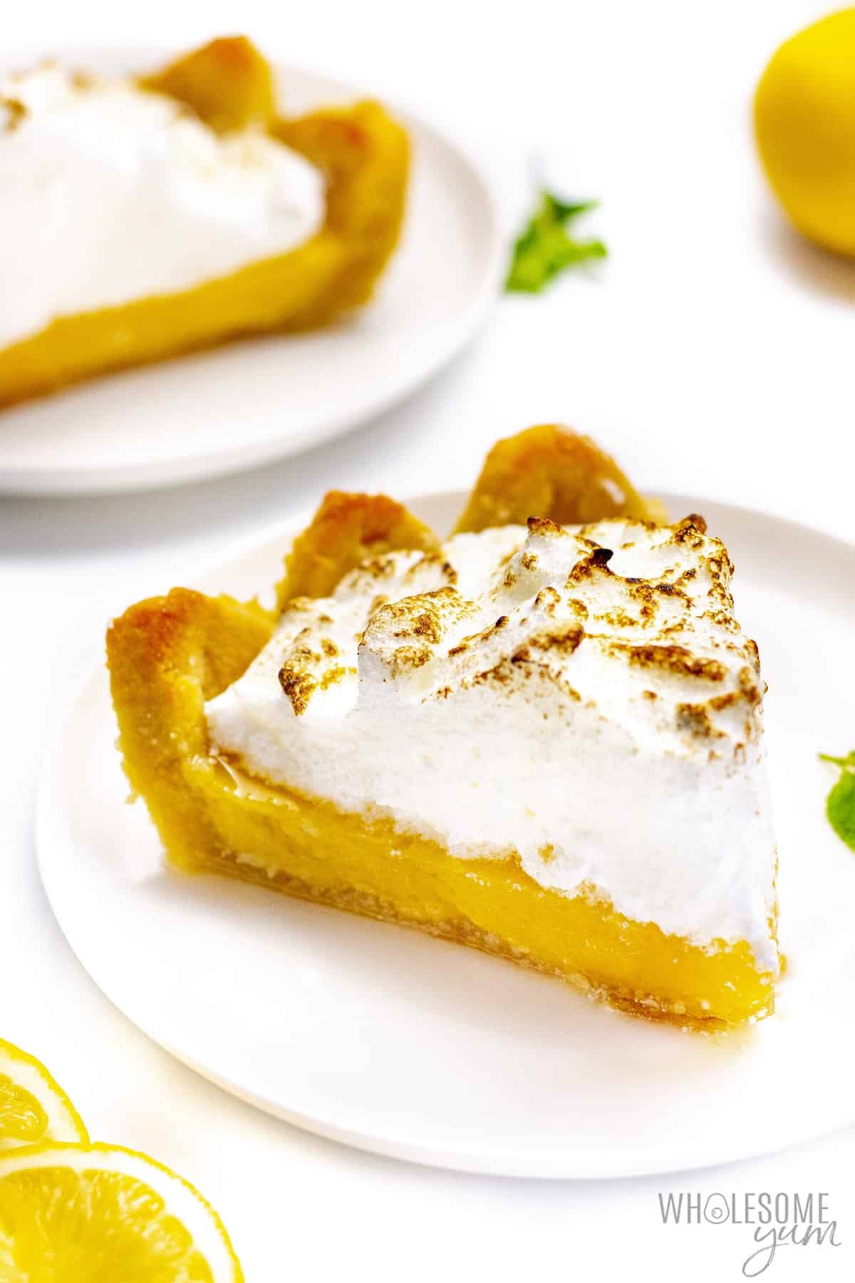 A piece of sugar-free lemon meringue pie on a plate with whole pie in the background.
