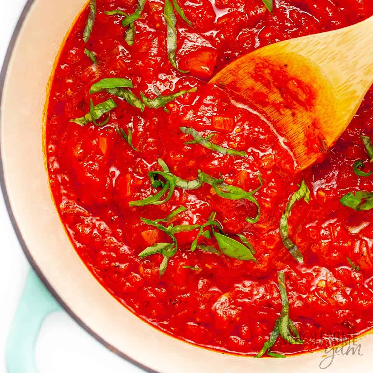 Keto marinara spaghetti sauce in a dutch oven with fresh basil ribbons and spoon.