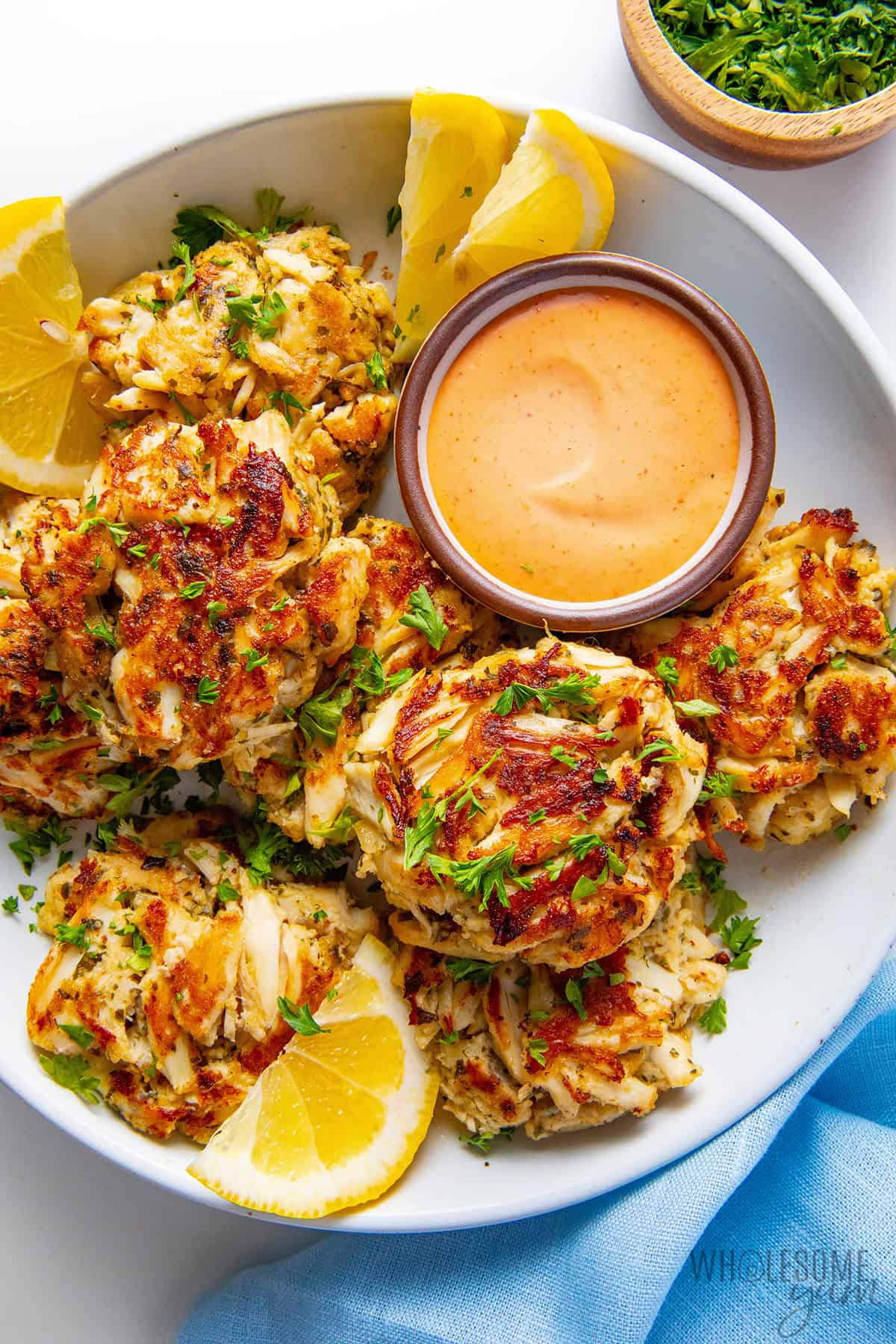 Crab cakes on a serving platter with spicy mayo and lemon wedges.