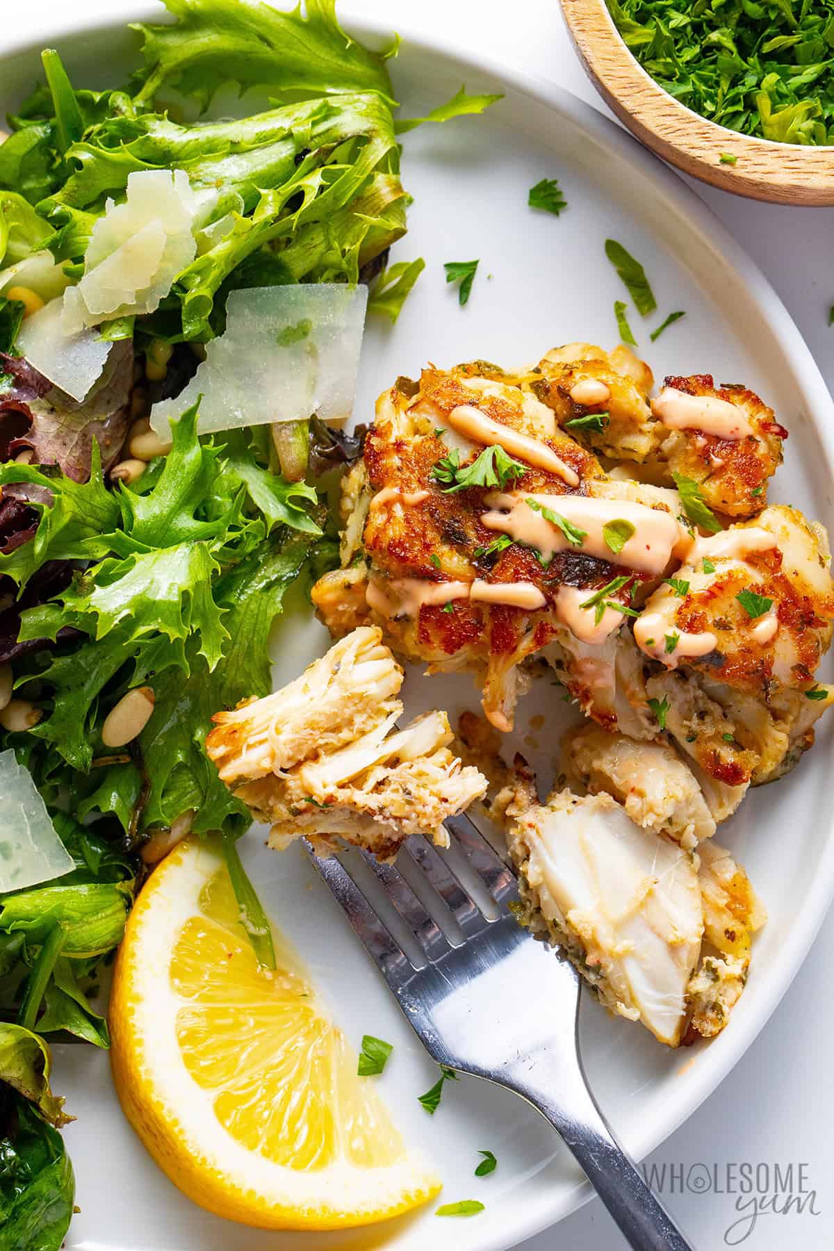 Maryland crab cake served with a drizzle of spicy mayo, a lemon wedge, and arugula salad.