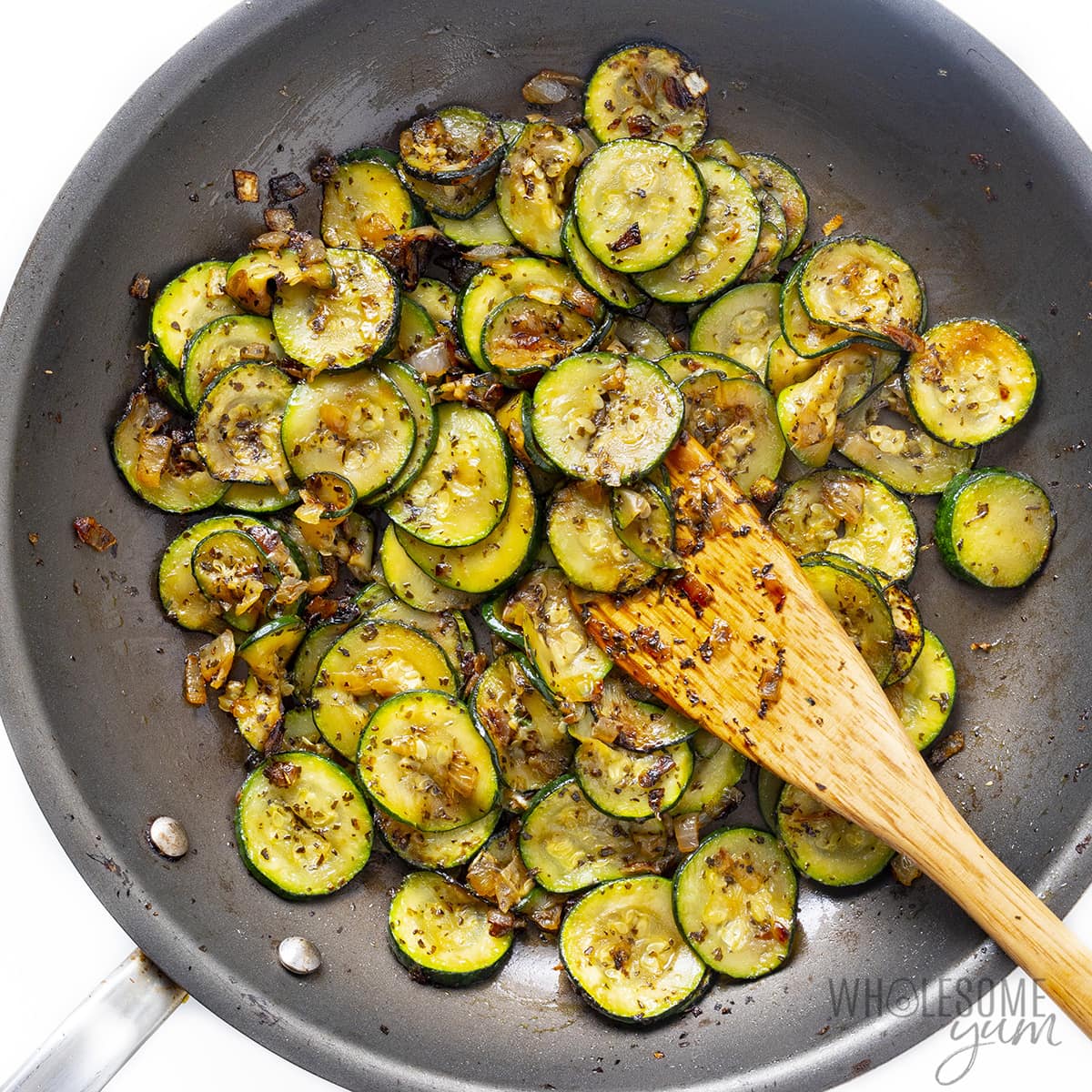 Onions cooking with sliced zucchini in a pan.