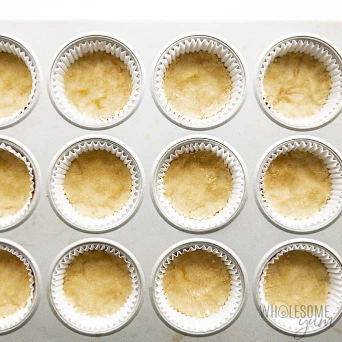 Small low carb cheesecake crusts pressed into a muffin tin.