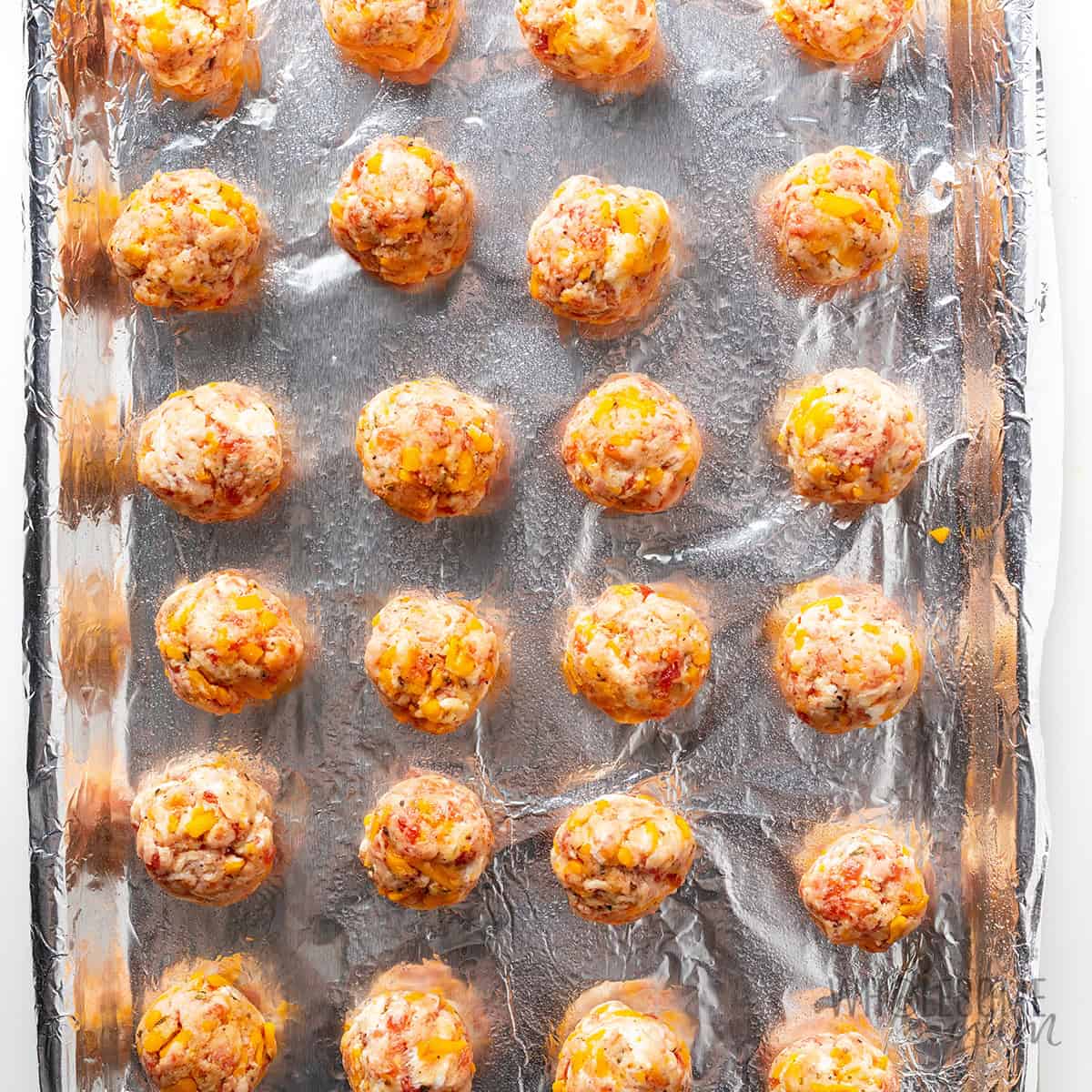 Raw sausage balls on a lined baking sheet.