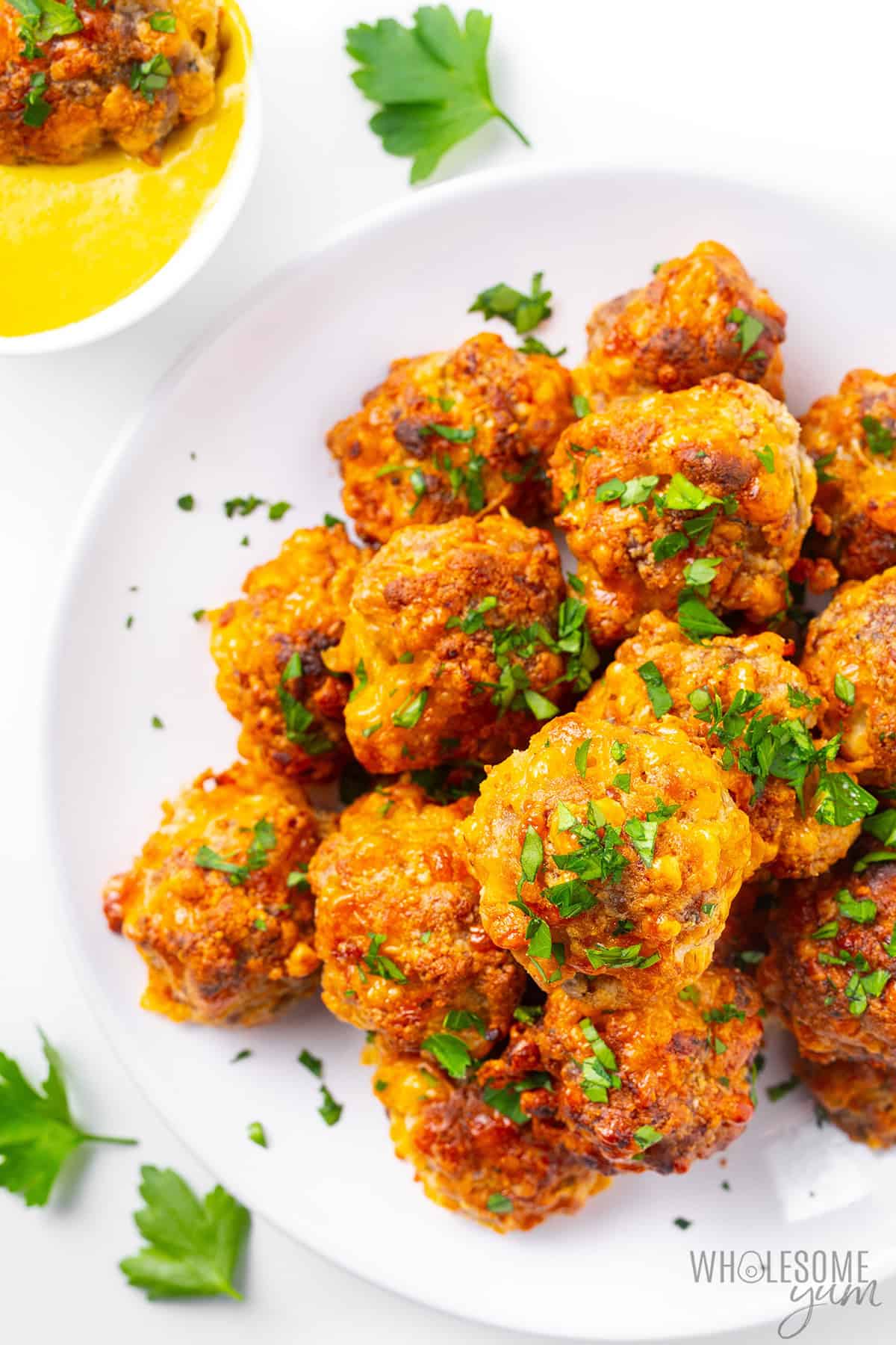 Cream cheese sausage balls on a serving plate with parsley and one dipped in honey mustard dipping sauce.