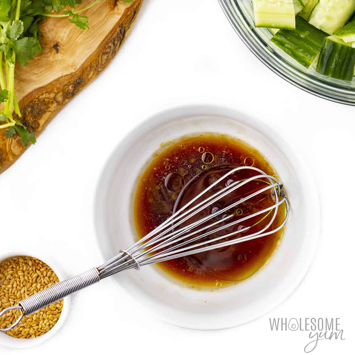 Smashed cucumber salad dressing in a bowl with whisk.