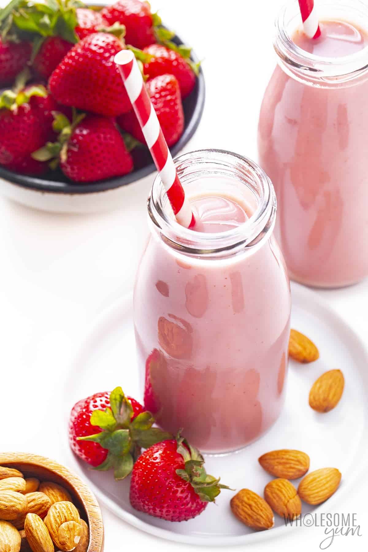 Glass bottles of strawberry almond milk next to bowl of strawberries.