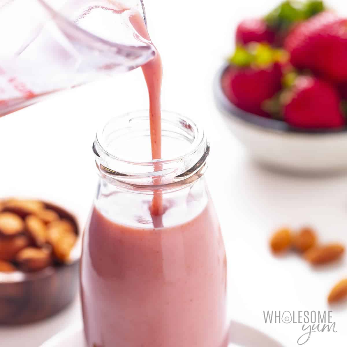 Strawberry almond milk pouring into glass bottle.