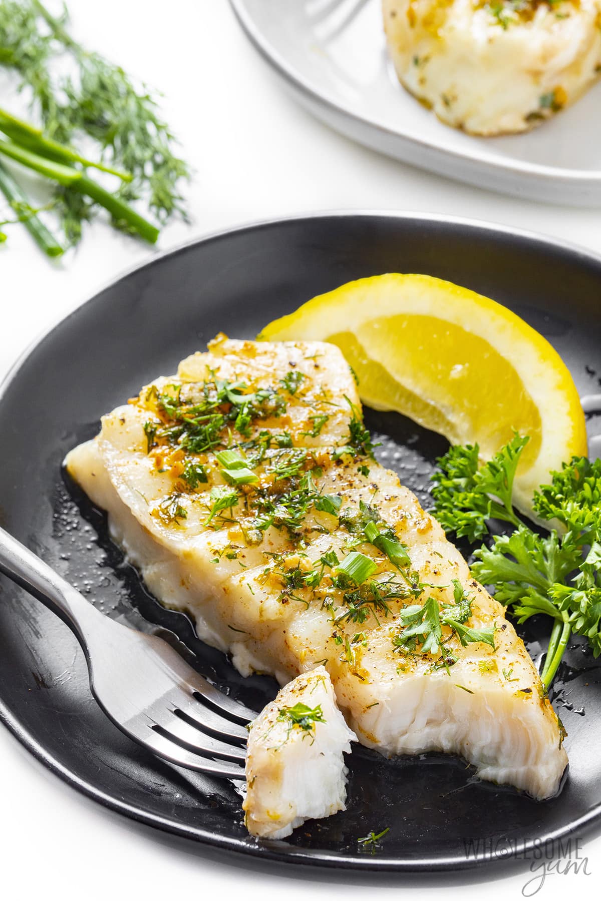 Baked halibut on a plate with a piece flaked using a fork.