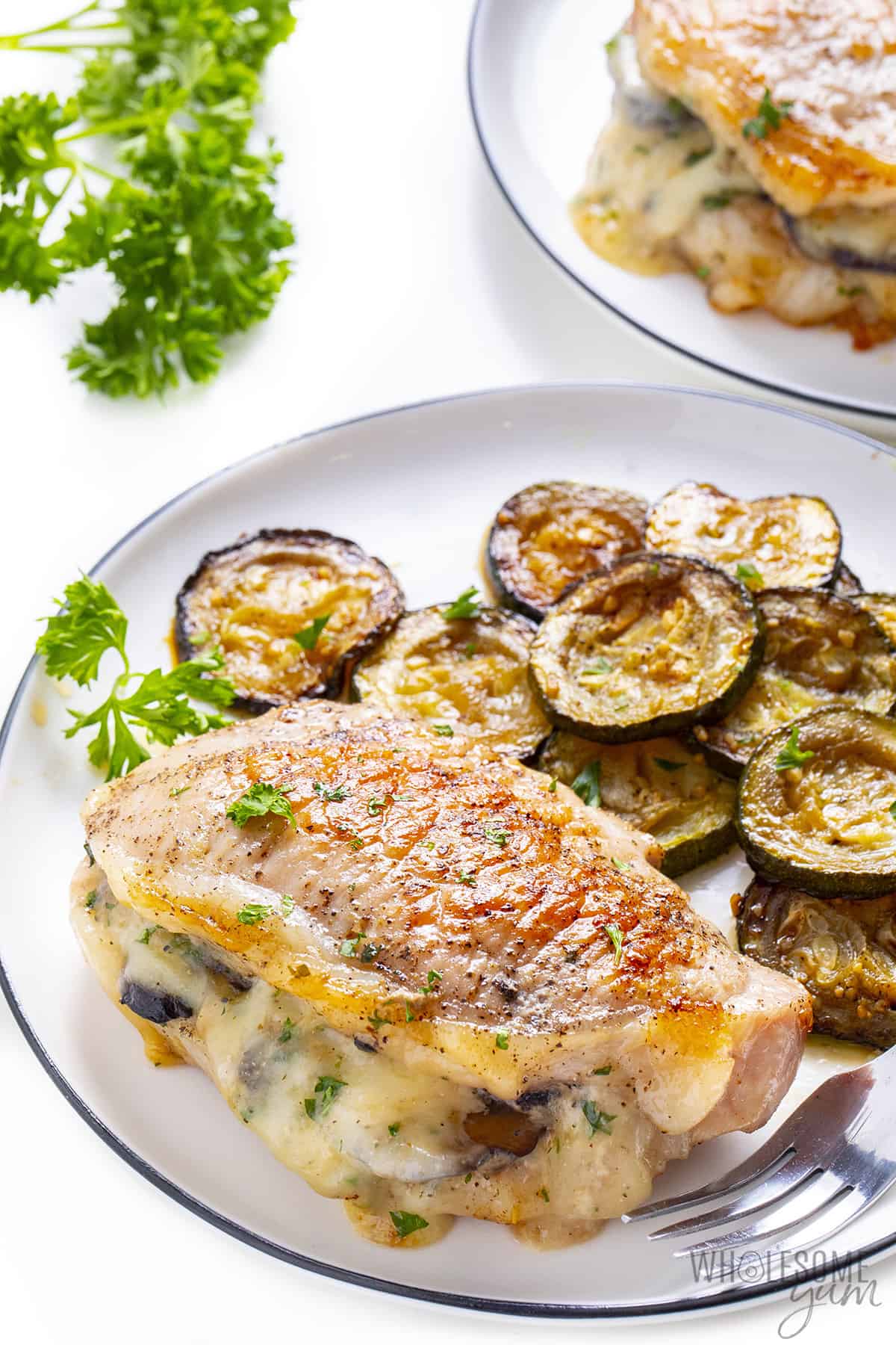 Plates of baked stuffed pork chops with side of sauteed zucchini.