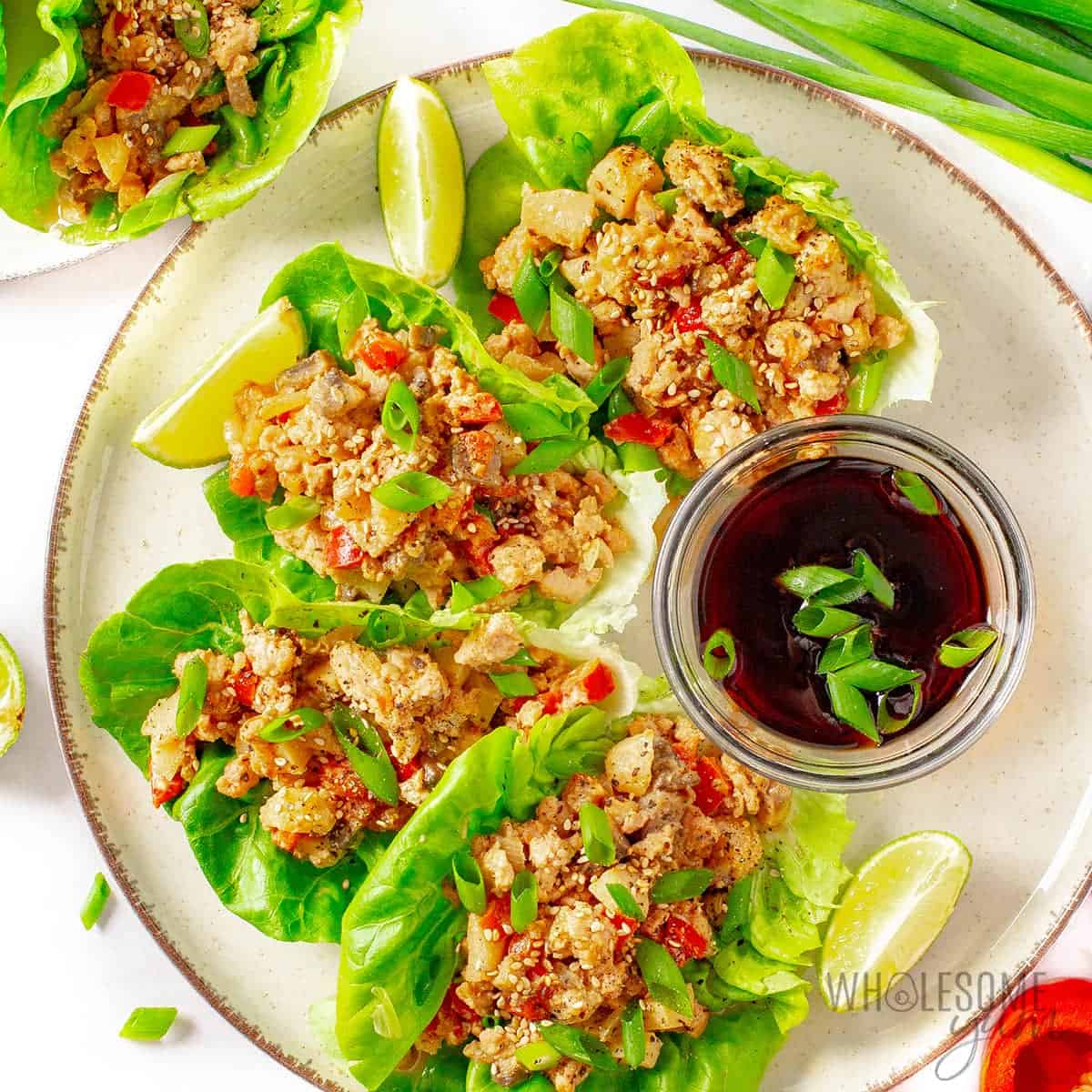 Healthy Asian chicken lettuce wraps on a plate with garnishes.