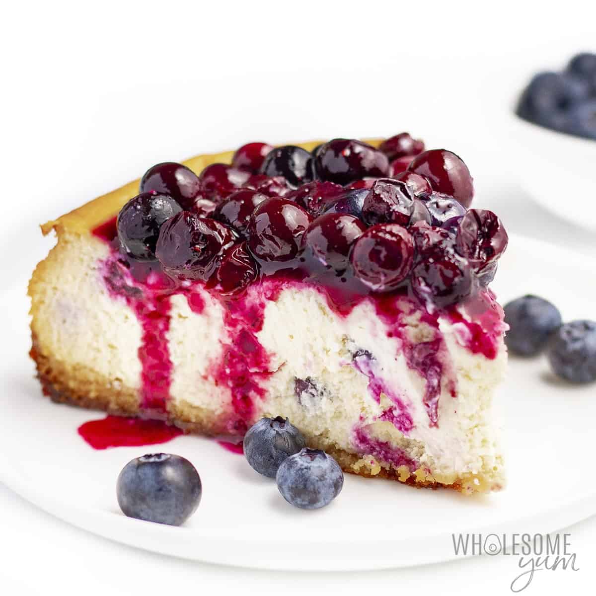 Low carb blueberry cheesecake slice on a plate with fresh berries on the side.