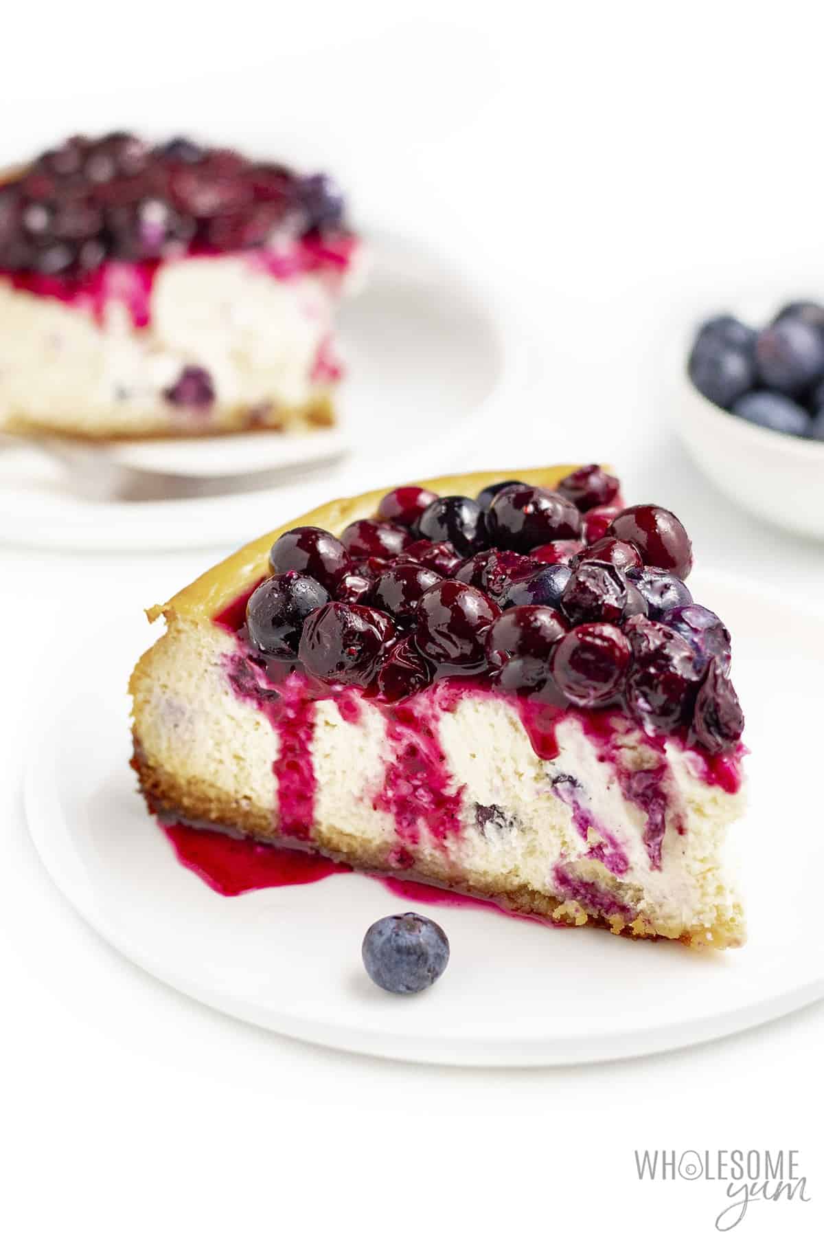 Slice of keto blueberry cheesecake on a plate with full cake in the background.