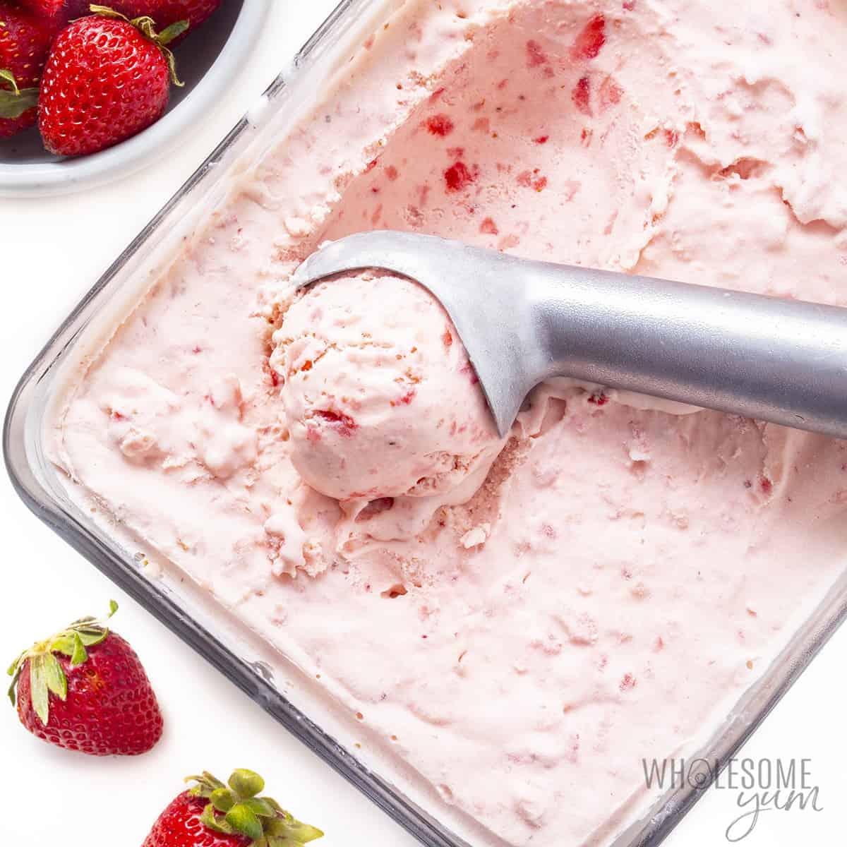 Ice cream in a container next to fresh strawberries.