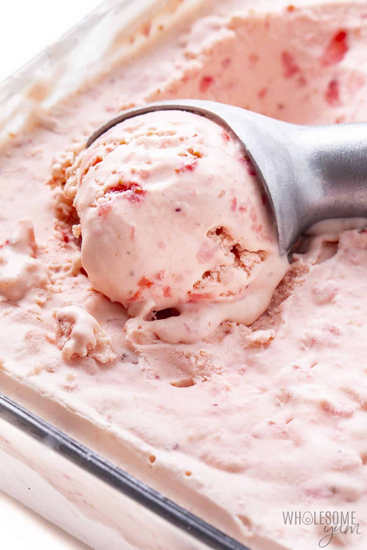 Strawberry keto ice cream in a glass container with scoop inside.