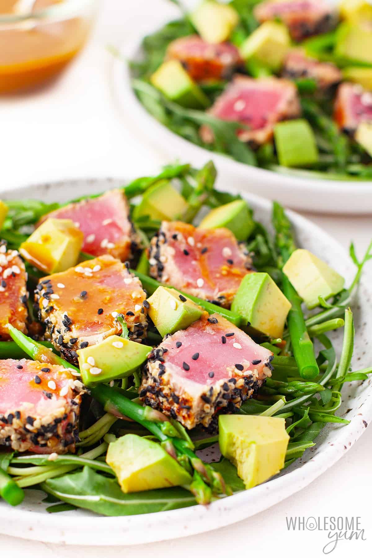 Ahi tuna salad on plates with dressing on the side.